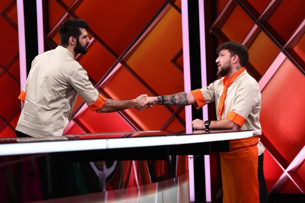 Chef Bogdan Iancu shaking hands with Richard Abou Zaki during Chefi la Cuțite 2025 — culinary battle, orange team moment